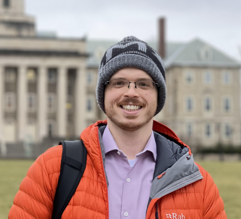 Cody Dennett- a young white man with short red facial hair. He wears wire framed glasses, a bright orange winter coat, and a black knit pompom hat