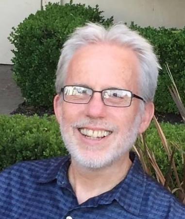 Headshot of John Moody; a white man with white hair and short white beard, wearing square glasses and smiling
