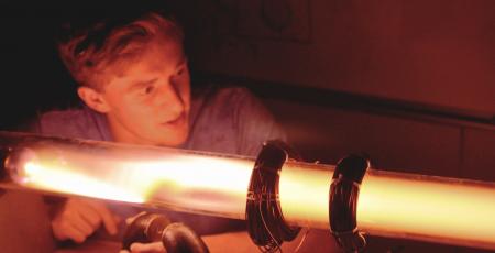  A man in a darkened room moving a large magnet along a linear plasma demo. 