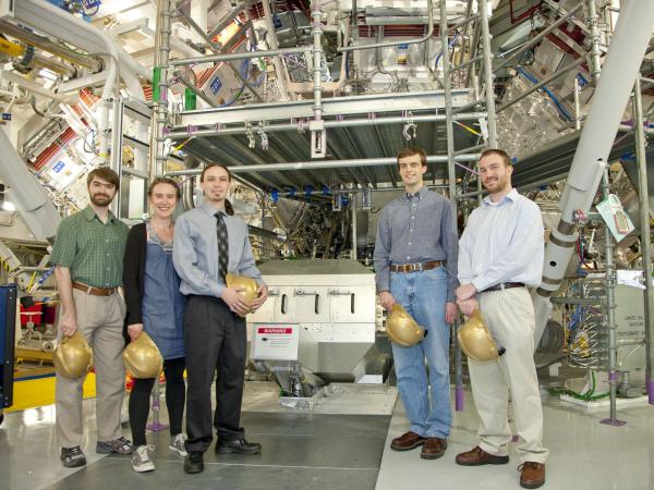 4 men and 1 woman scientist stand in front of machinery that features a diagnostic knows as Magnetic Recoil neutron Spectrometer (MRS).