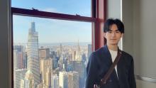 Shoma Akamatsu stands to the right of the photo. A window to his left shows a city skyline