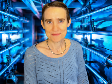 A scientist in a blue sweater posed in front of the National Ignition Facility lasers.